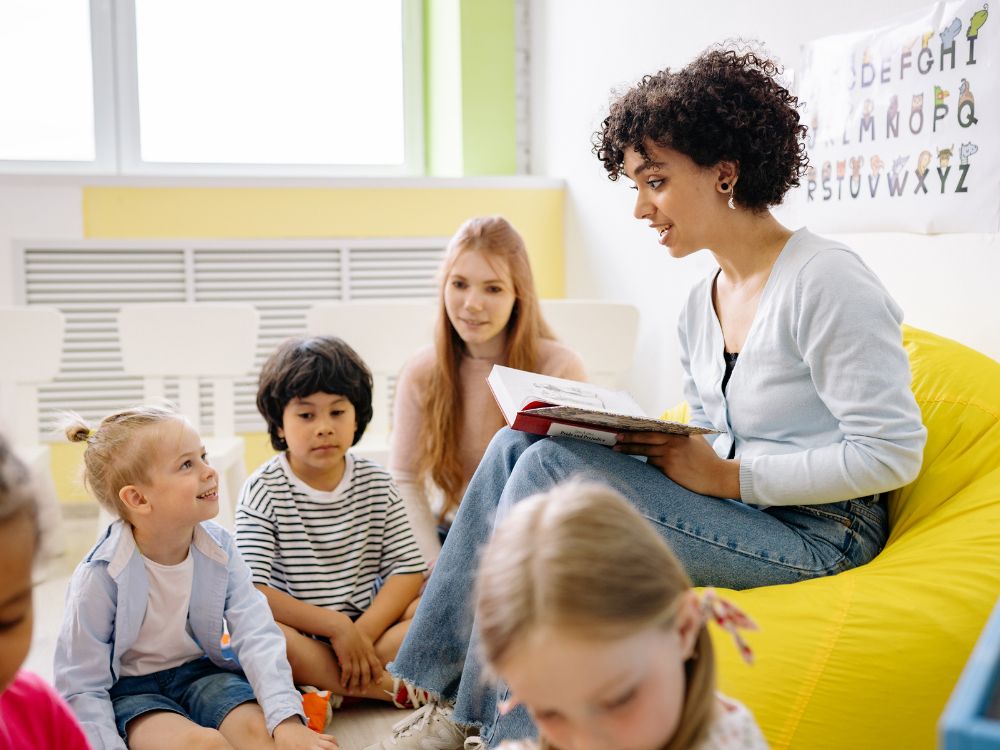 Professora lendo livro para crianças em sala de aula, representando como ser professor infantil e a importância da interação no aprendizado.